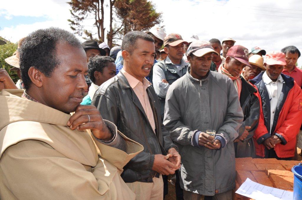 Frère Pascal, Mr. le Maire et le Chef de chantier arrose d'eau bénite et de rhum le terrain et les matériaux avant le lancement du chantier de construction du bâtiment à Antanety - Madagascar.